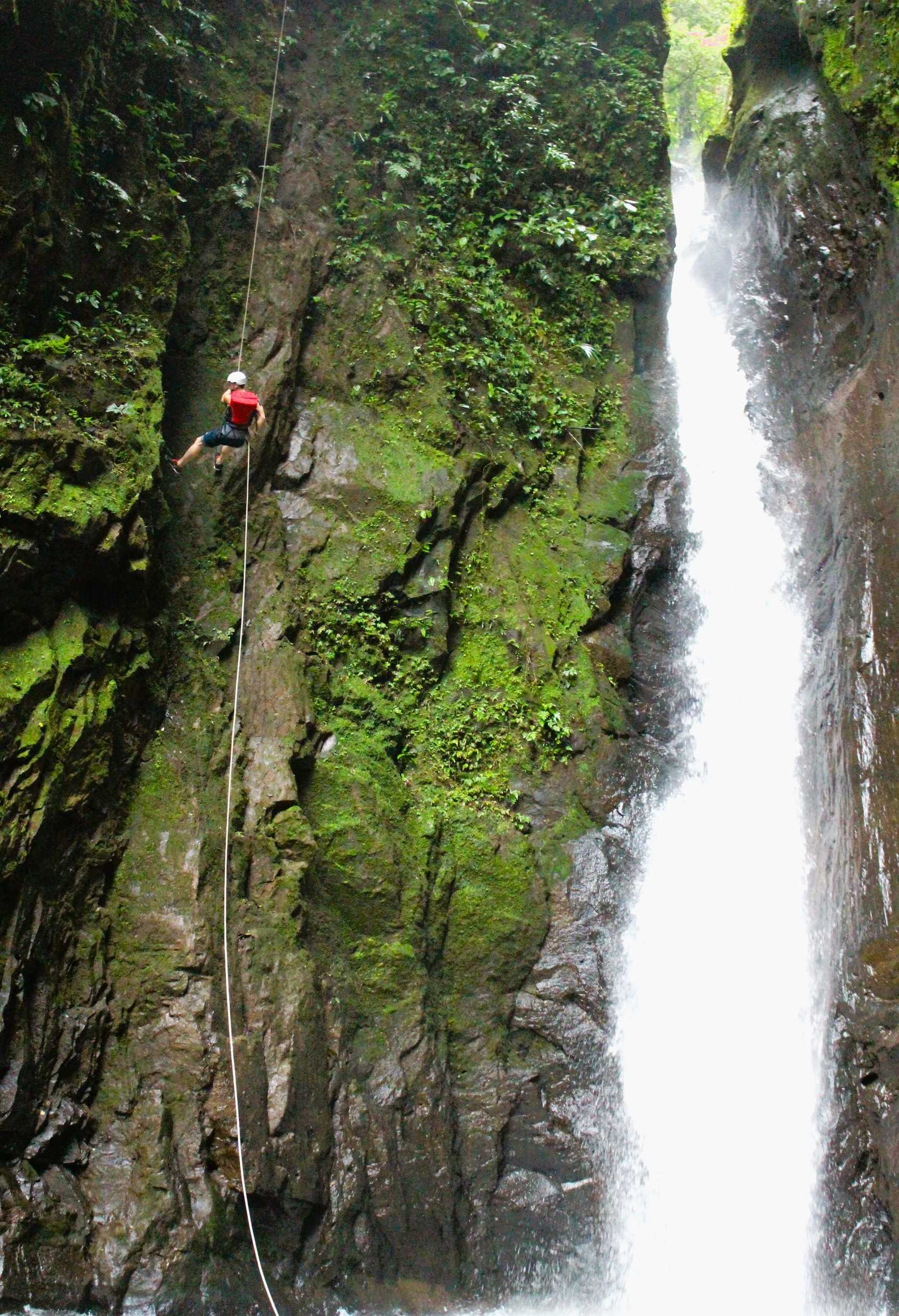 A man doing rappel down a cliff beside a waterfall