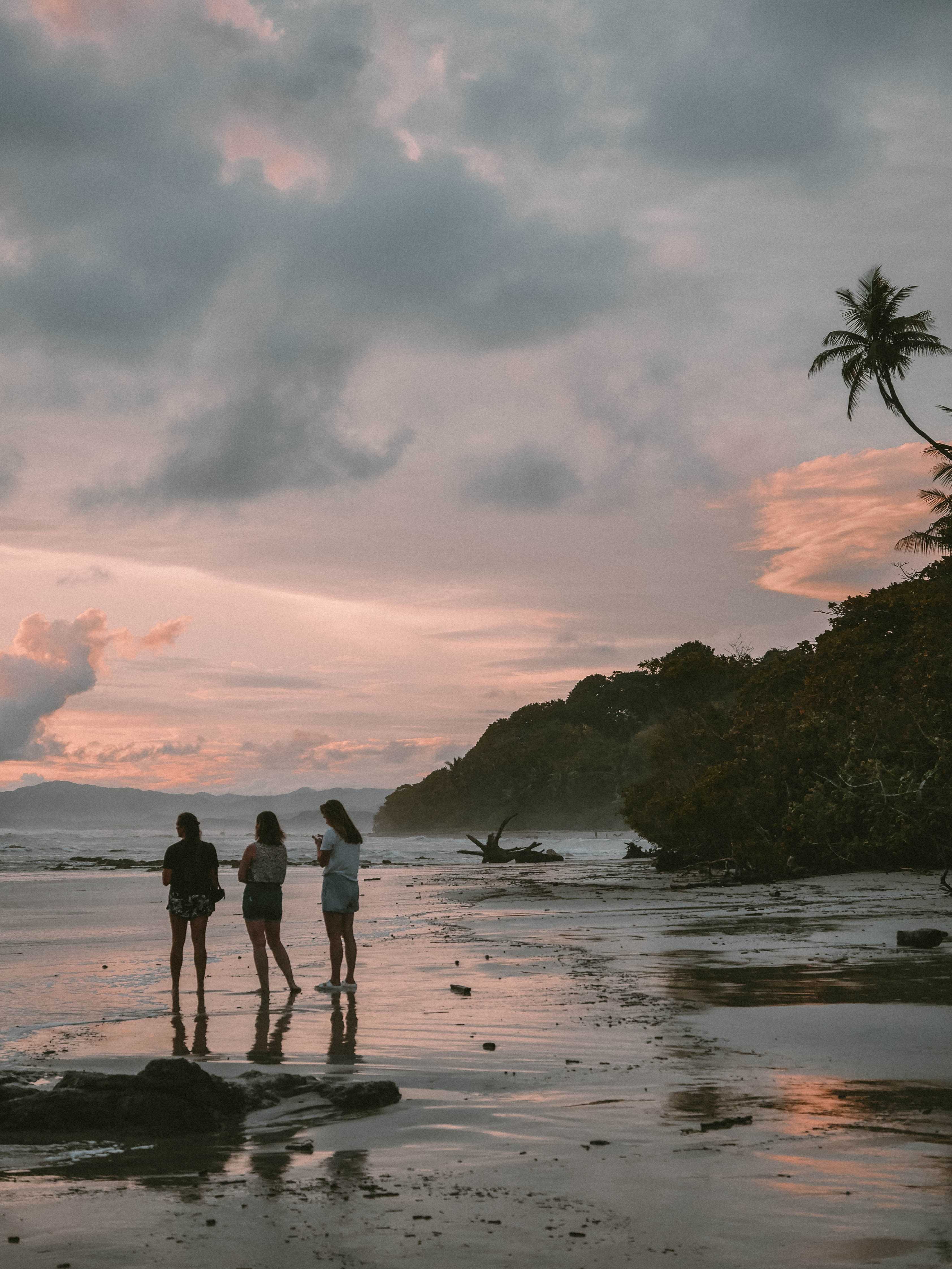 A group of girls standing at the beach at sunset